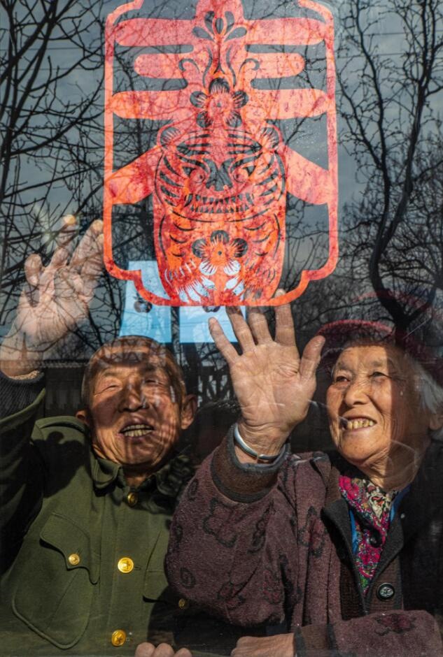 臘月里，霍州市師莊鄉(xiāng)馮南垣村村民師榮光(左)在災(zāi)后重建的新家里貼窗花。(霍州市委宣傳部供圖)