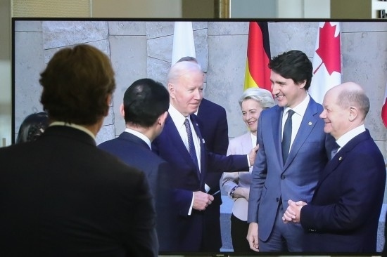 2022年3月24日，在比利時布魯塞爾的北約總部，一名男子觀看屏幕上美國總統拜登（右四）、歐盟委員會主席馮德萊恩（右三）、加拿大總理特魯多（右二）、德國總理朔爾茨（右一）出席七國集團峰會合影儀式的畫面。新華社記者鄭煥松攝