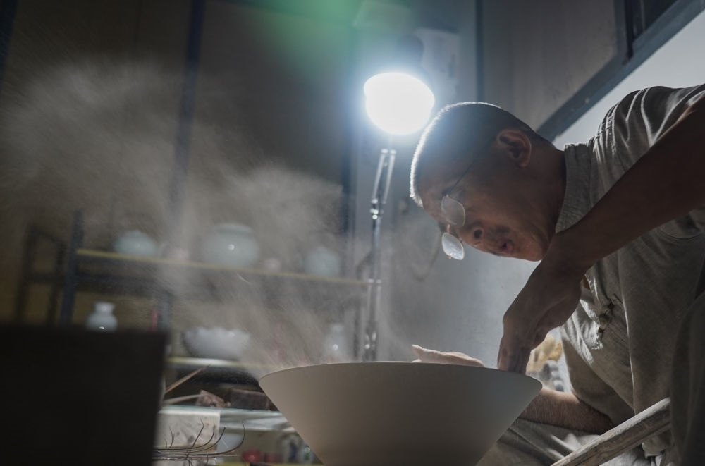 ↑ 在景德鎮(zhèn)，手工匠人吹去坯內(nèi)的泥土（2021年7月14日攝）。