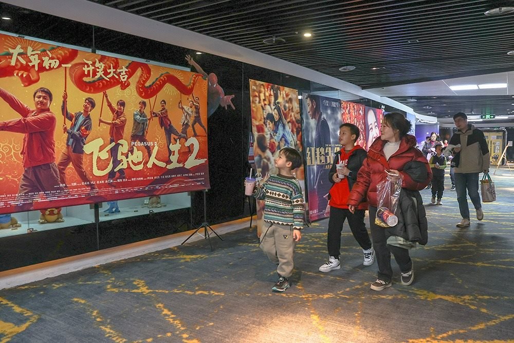 △ 2024年2月16日，在江西贛州一家電影院，觀眾從春節(jié)檔電影的宣傳展板前走過。