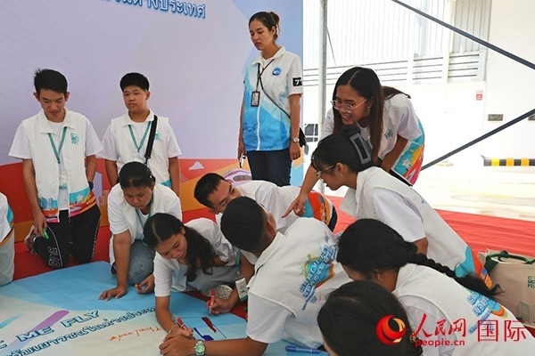 泰國學(xué)生在開營儀式展板上繪制圖案。人民網(wǎng)記者 白元琪攝